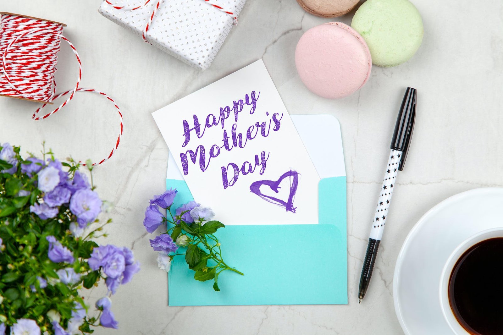 happy mothers day card beside pen macaroons flowers and box near coffee cup with saucer